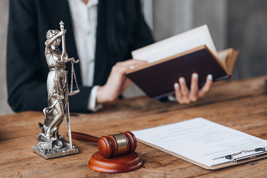 Lawyer holding law book with gavel and lady liberty statue on desk for Criminal Defense Lawyer